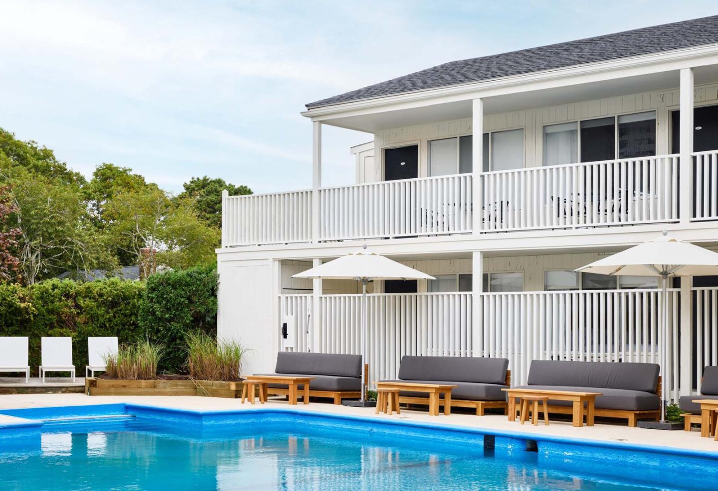 Two-story white building, pool, lounge chairs, and umbrellas.