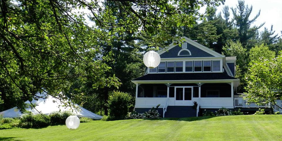 Large house with a porch, surrounded by trees and a grassy lawn.