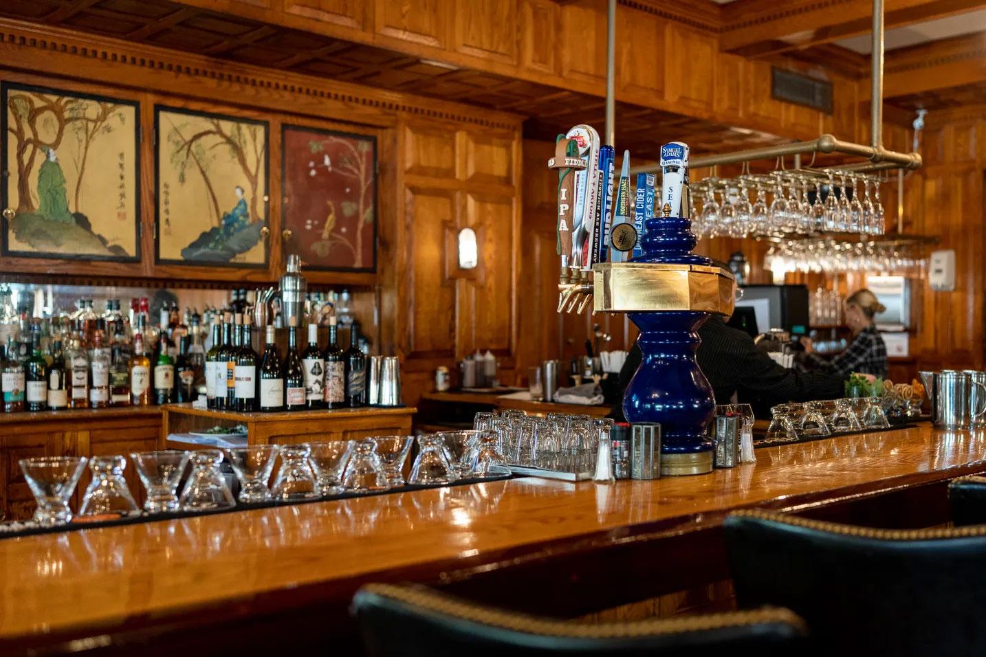 Cozy wooden bar with bottles, glasses, and a person behind the counter.