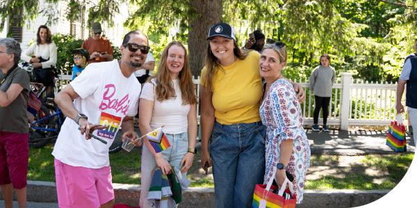 Four people smiling with pride flags at an outdoor event.