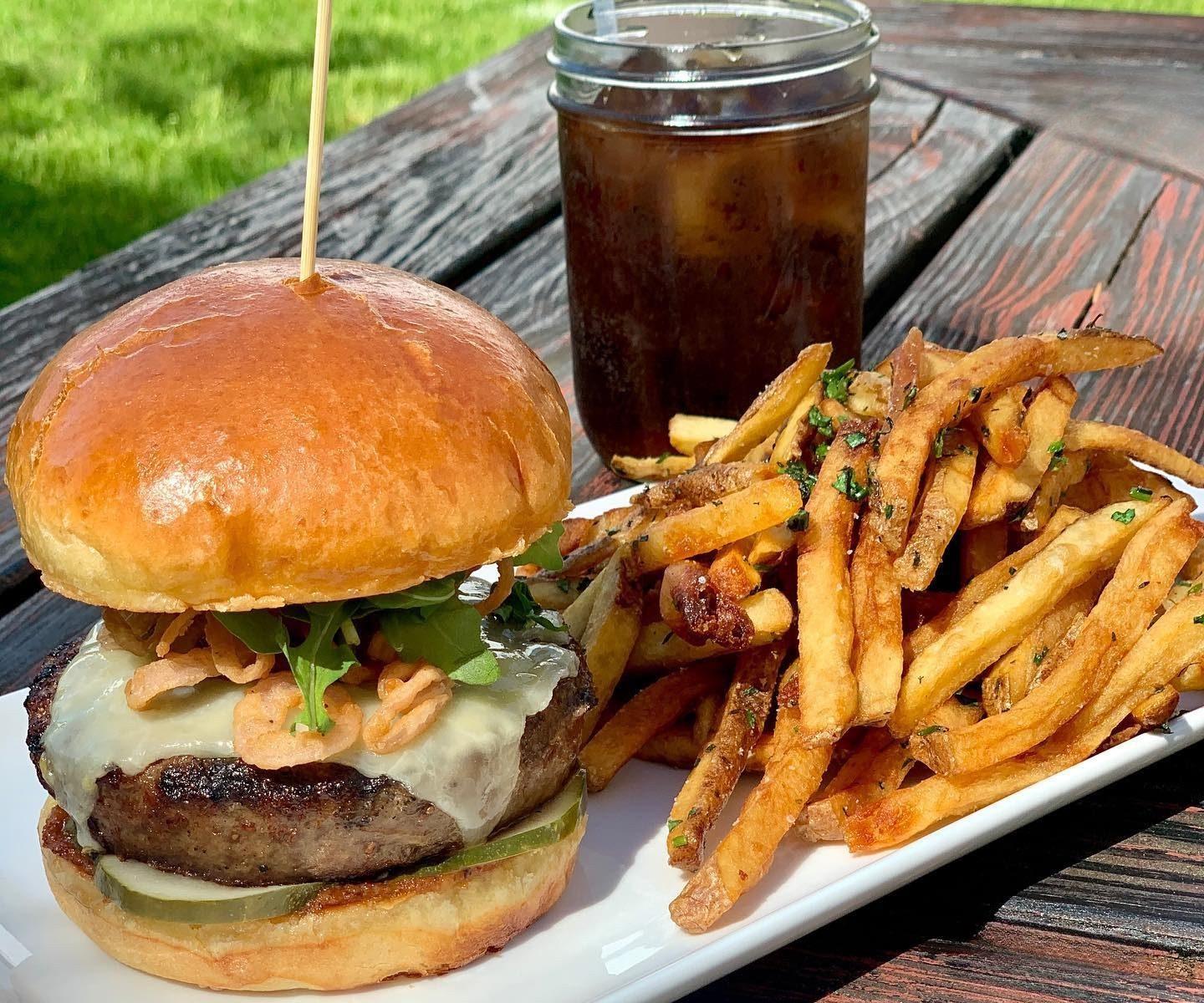Burger with fries and iced drink on a wooden table outdoors.