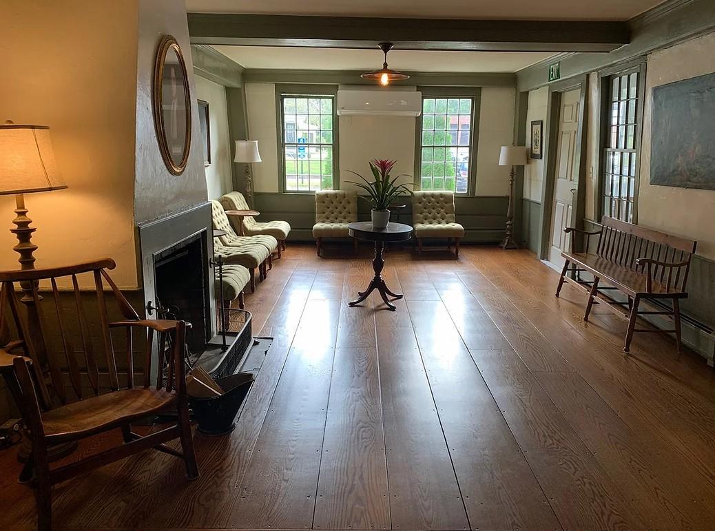 Cozy living room with wooden floor, chairs, and two sofas near windows.