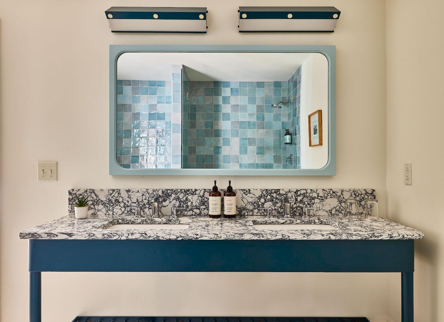 Bathroom vanity with blue mirror and lights, and tiled wall reflection.