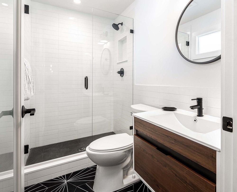 Modern bathroom with a glass shower, round mirror, and dark wood vanity.