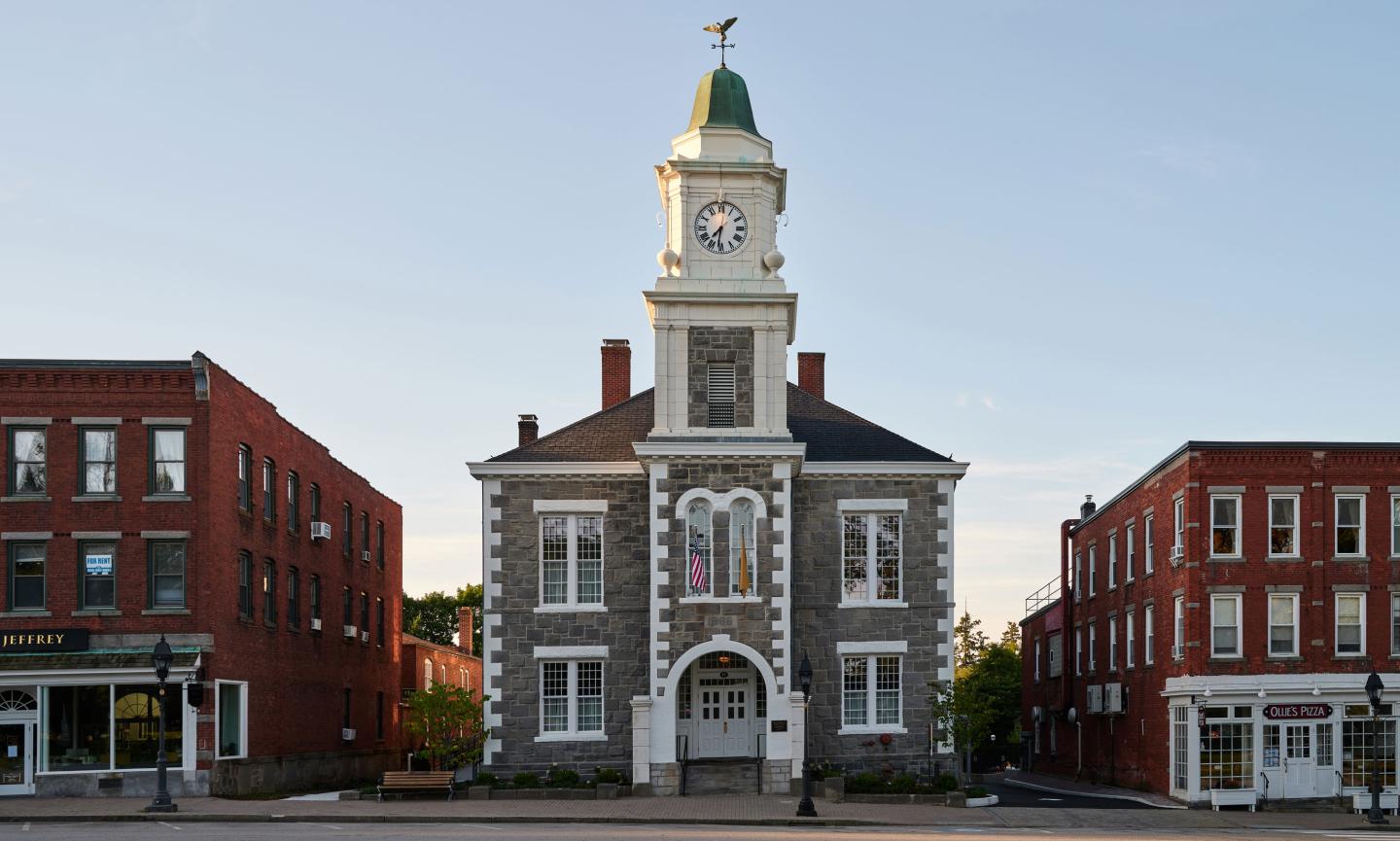 Historic stone courthouse with a clock tower at sunset, flanked by red brick buildings.