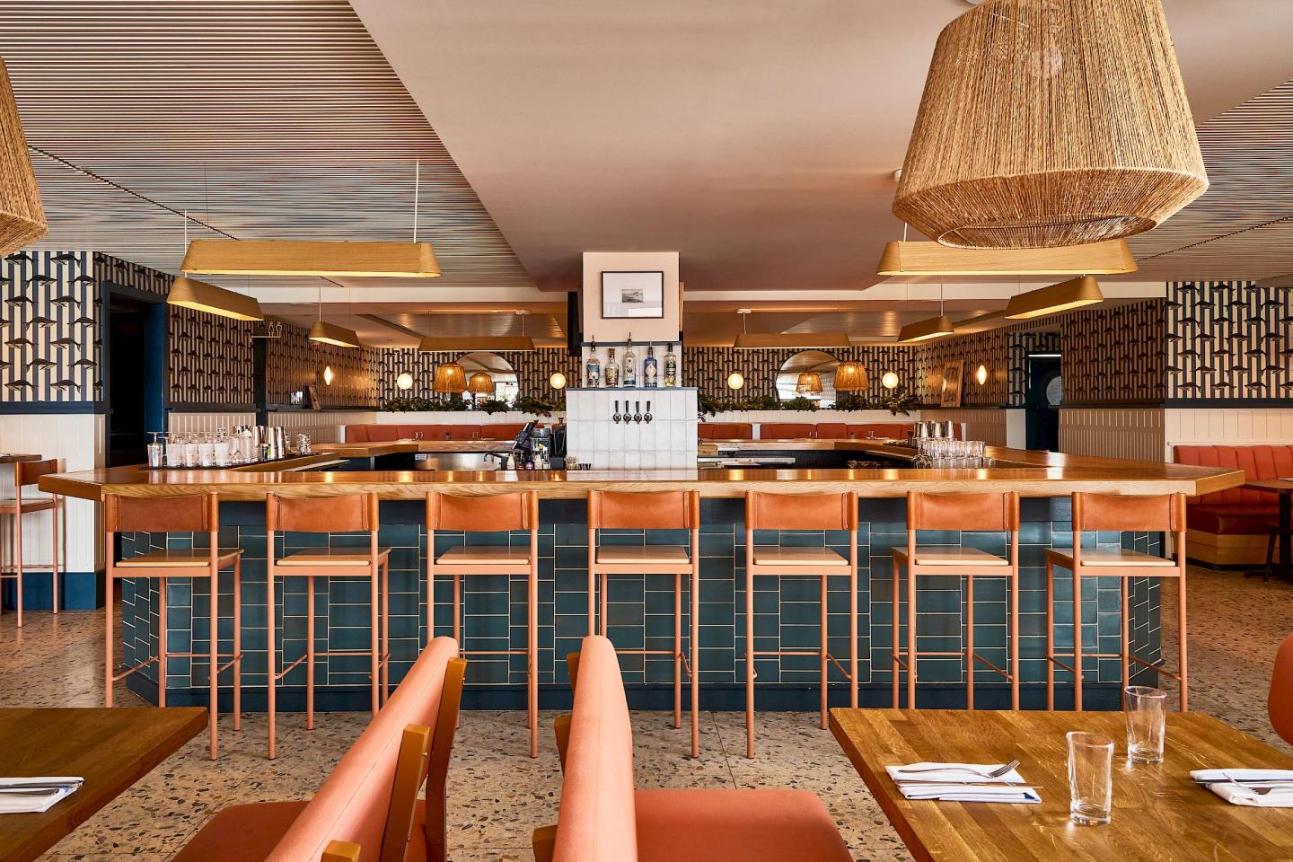 Chic restaurant interior with a wooden bar and wicker lampshades.