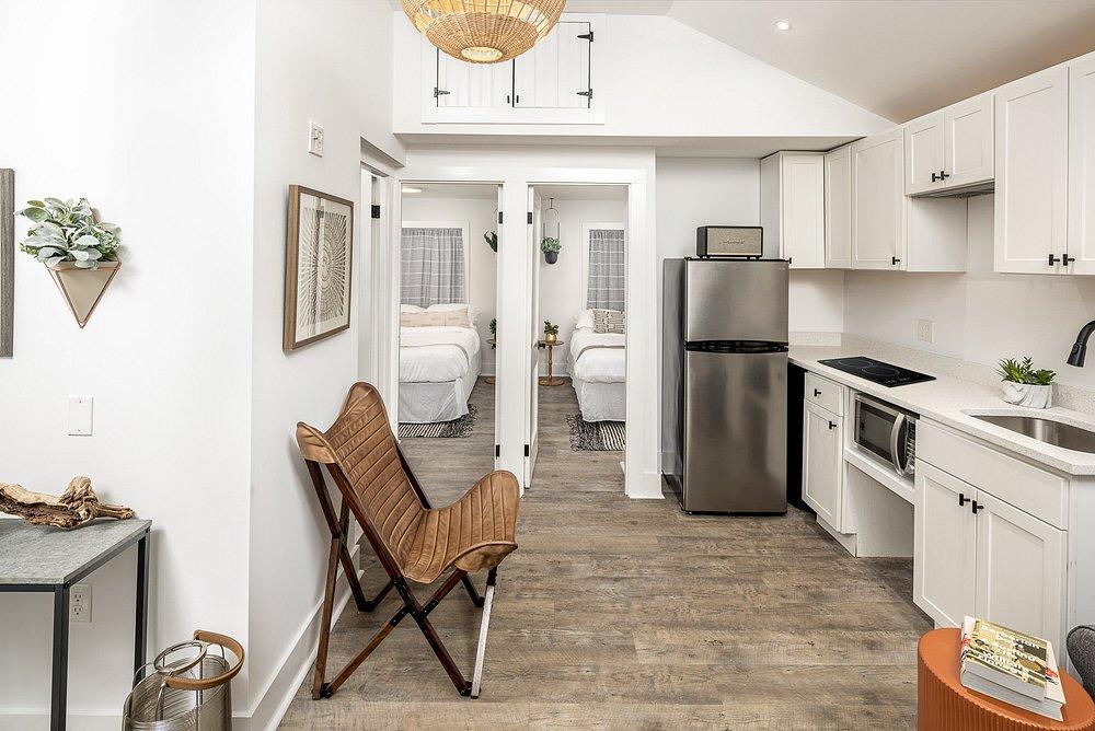 Bright kitchen with white cabinets, stainless steel appliances, wooden floor, and a wicker chair.
