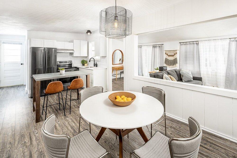 Modern kitchen and dining area with white walls, gray chairs, and a round table with fruit.