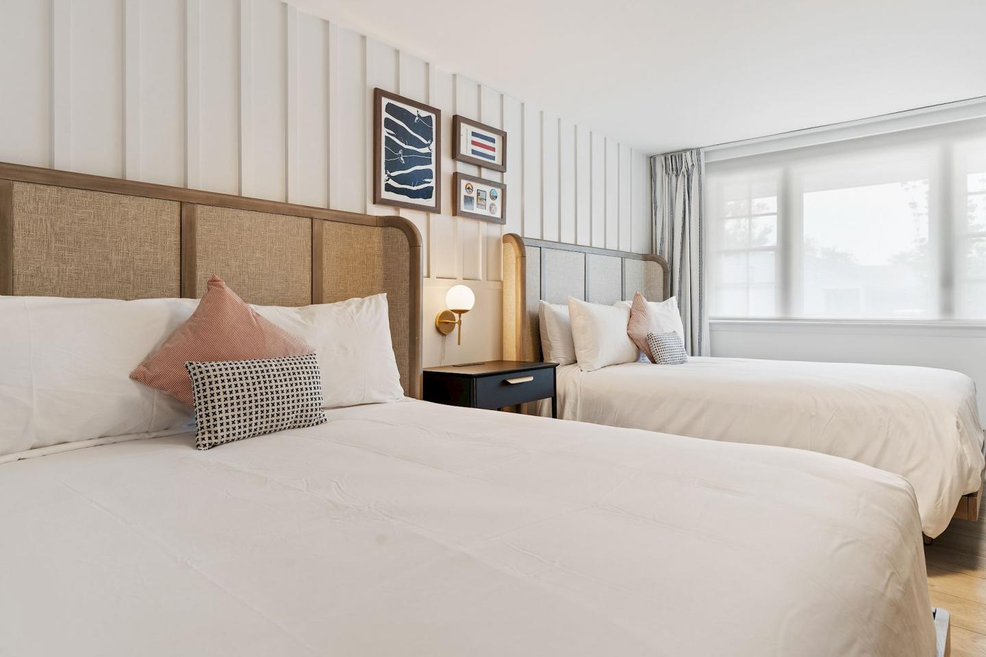 Two neatly made beds in a bright hotel room with wall art above.