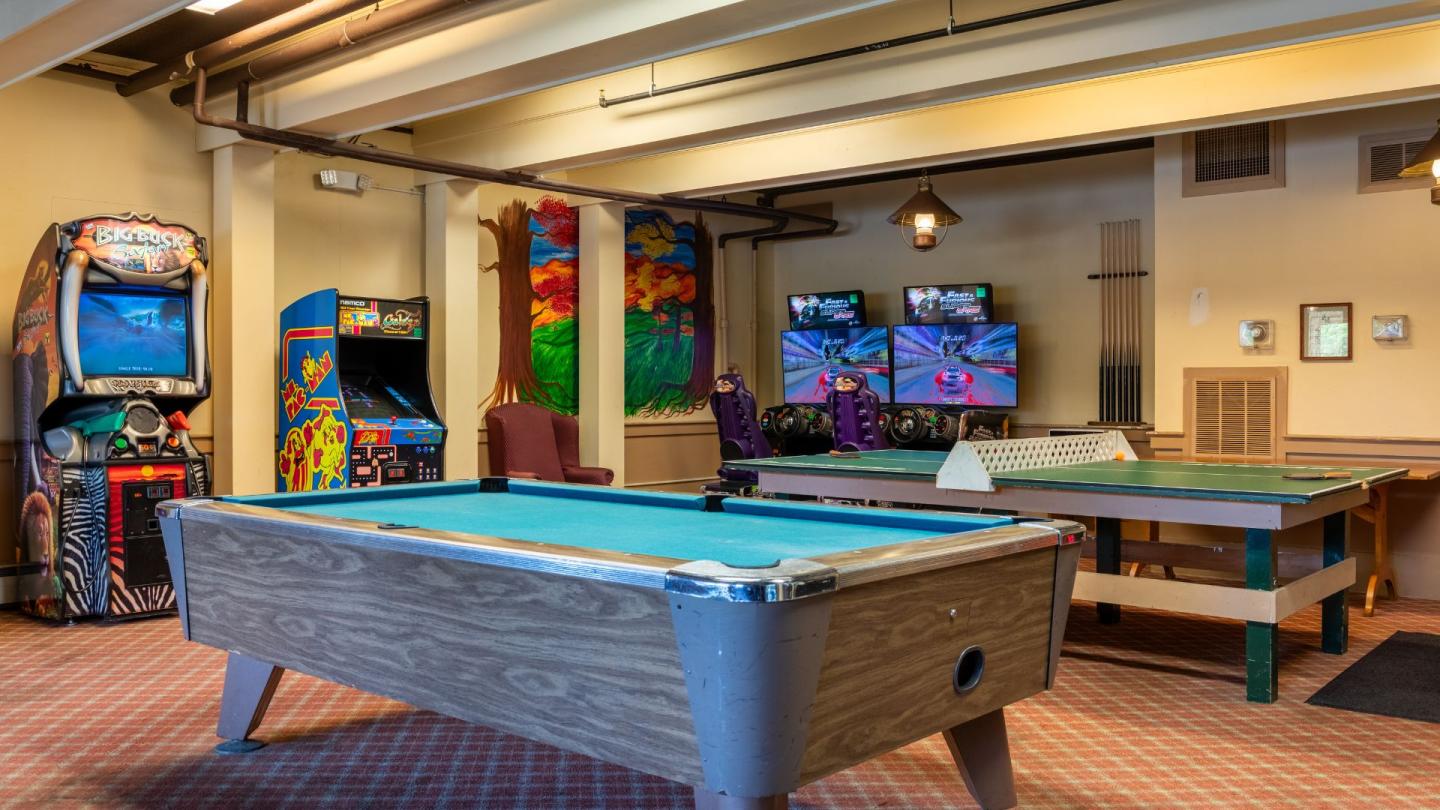 Pool table in a well-lit game room with arcade machines and flat-screen TVs.
