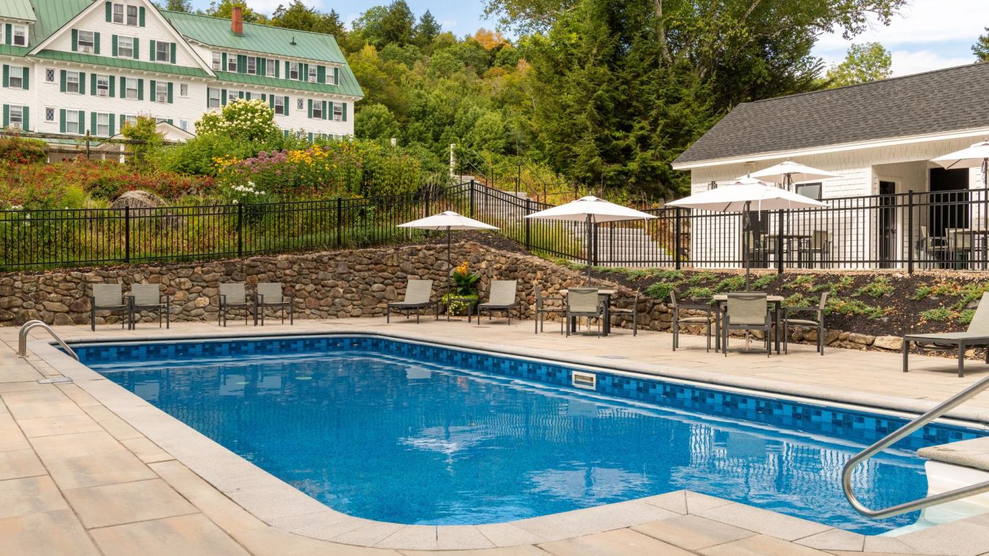 Outdoor pool with loungers and umbrellas, surrounded by greenery.