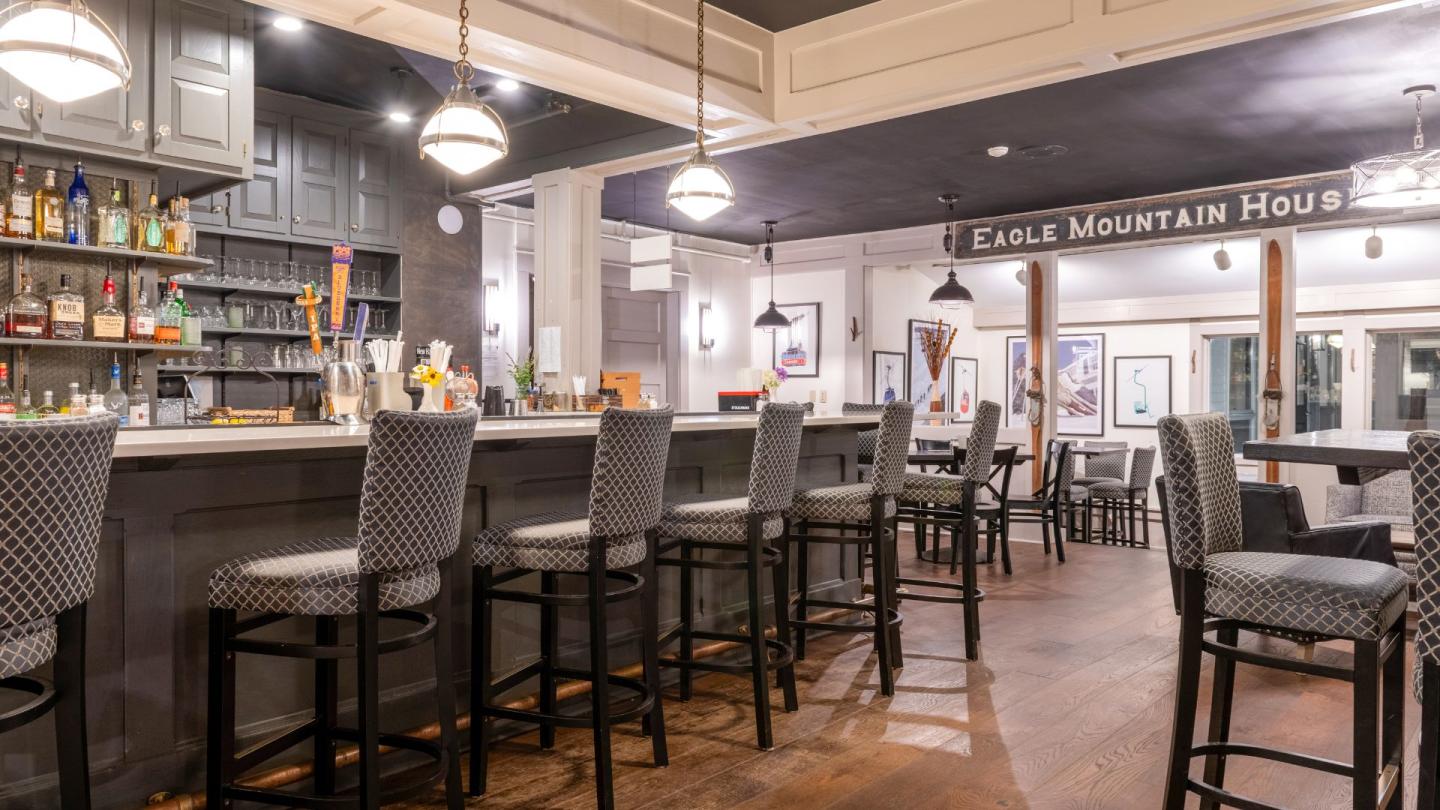 Bar interior with high chairs, wooden floor, and hanging lights.