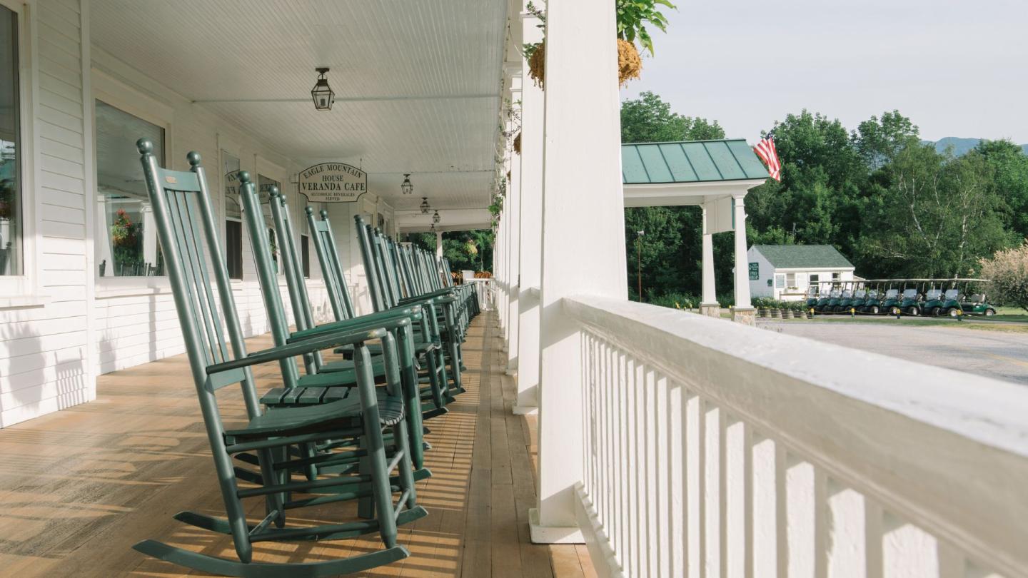 Row of green rocking chairs on a sunny porch.