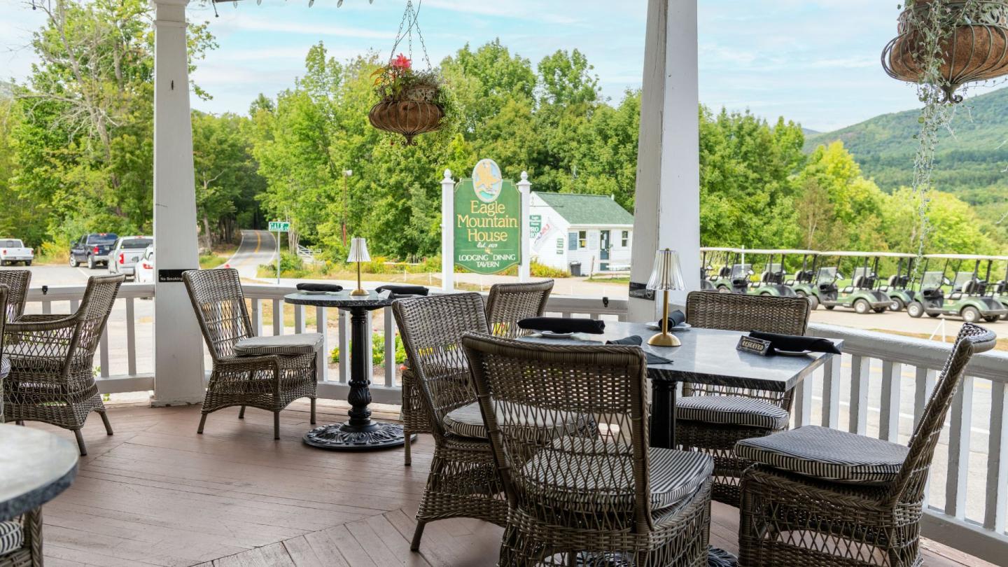 Outdoor patio with wicker chairs and tables, overlooking a scenic green landscape.