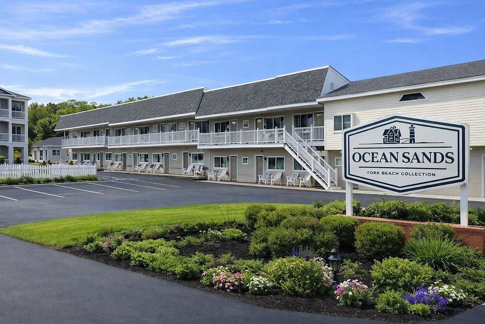 Oceanfront motel with gray roof, lush landscaping, blue sky, and Ocean Sands sign.