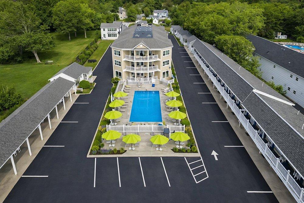 Aerial view of a hotel with a central pool, surrounded by parked cars and green umbrellas.