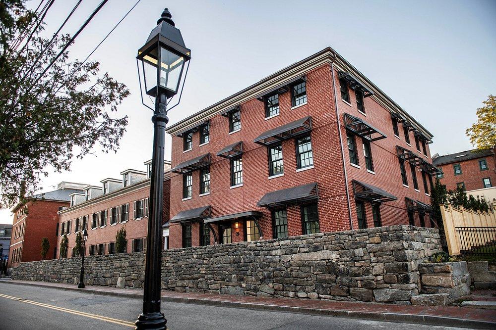 Brick building with green window awnings and stone wall, streetlamp in foreground.