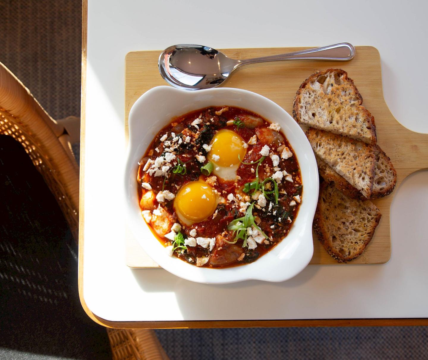 Shakshuka with eggs and toast on a wooden board.