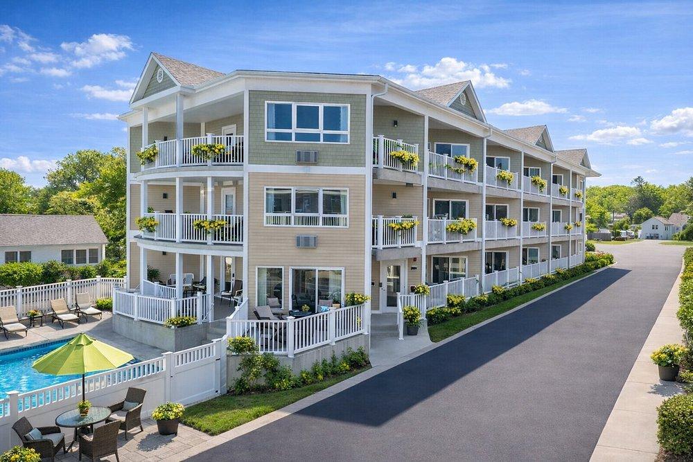 Three-story beige apartment building with balconies and a pool, sunny day.