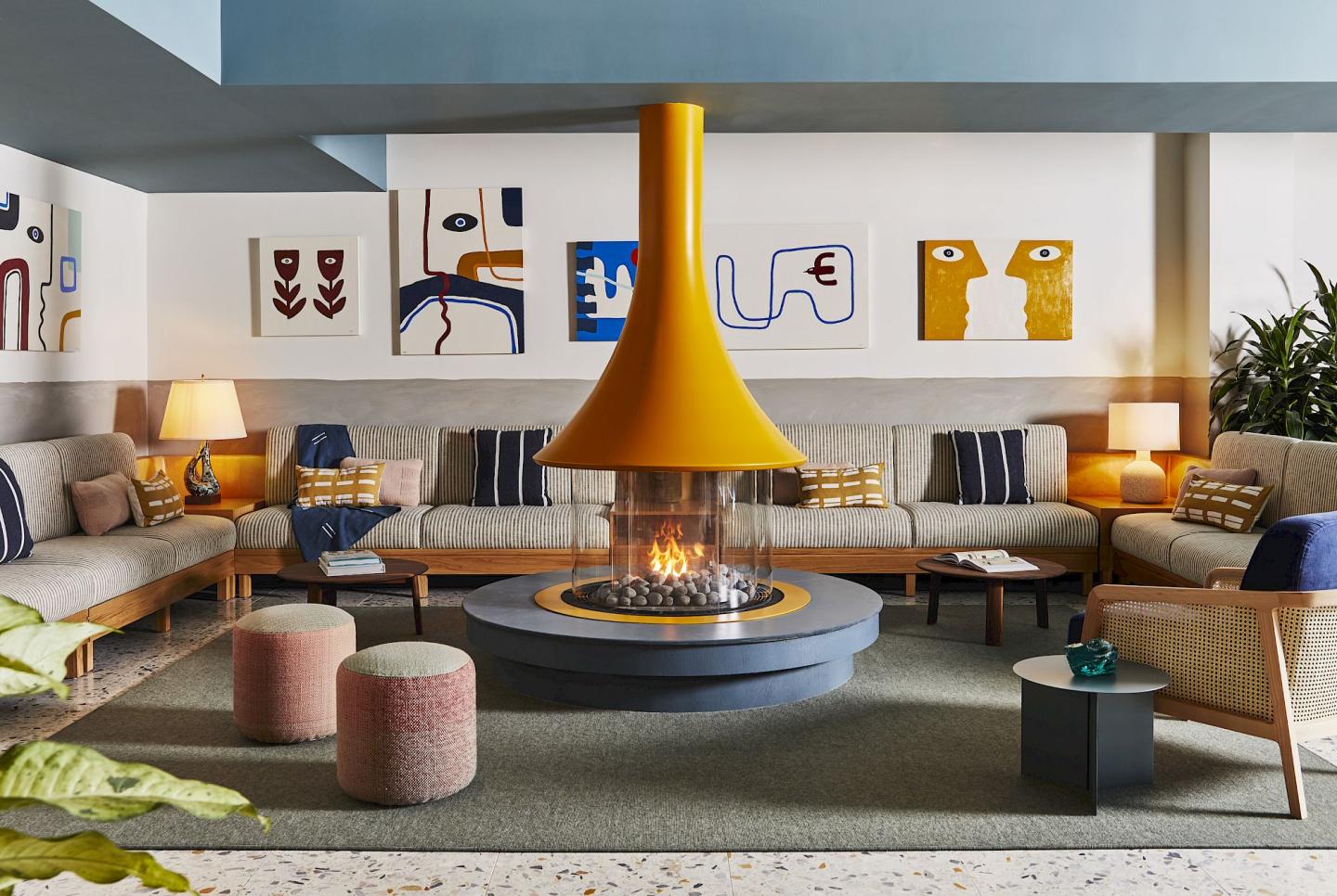 Colorful lounge with central yellow fireplace, modern sofas, and abstract art on walls.