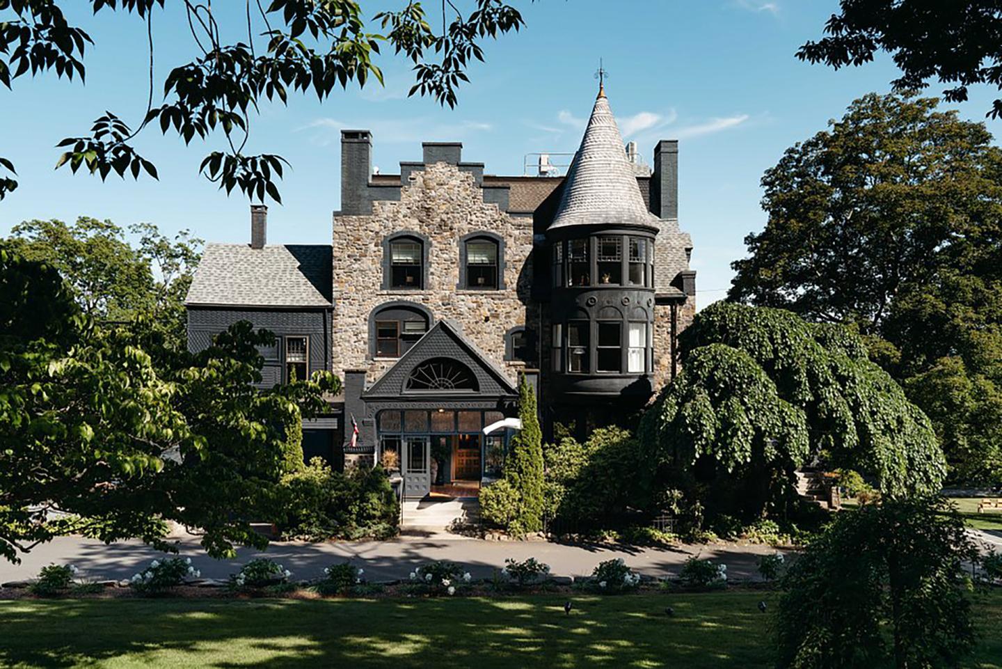 Stone mansion with turret surrounded by lush greenery under a blue sky.