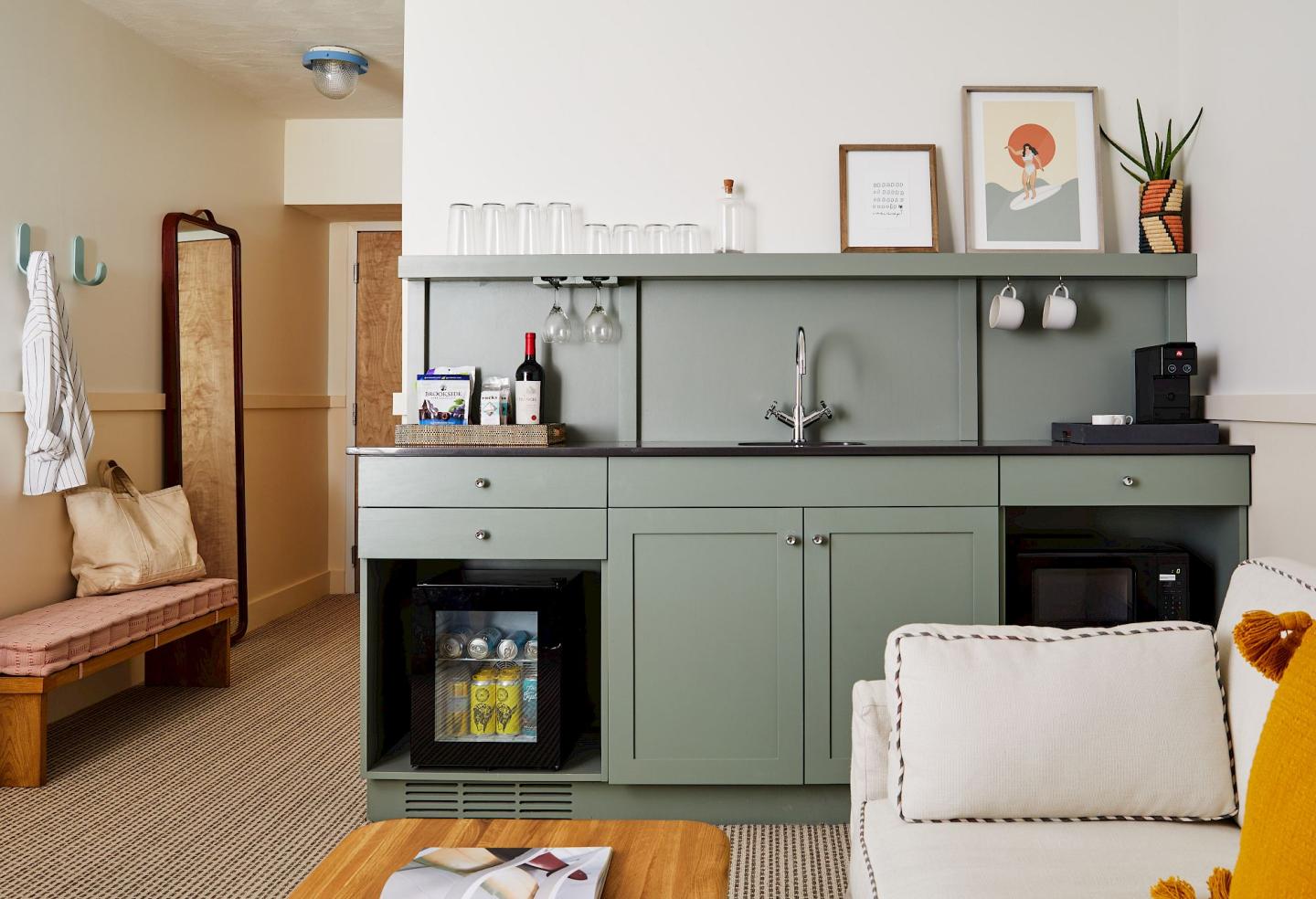 Small kitchenette with green cabinets, a mini-fridge, and coffee maker in cozy room.