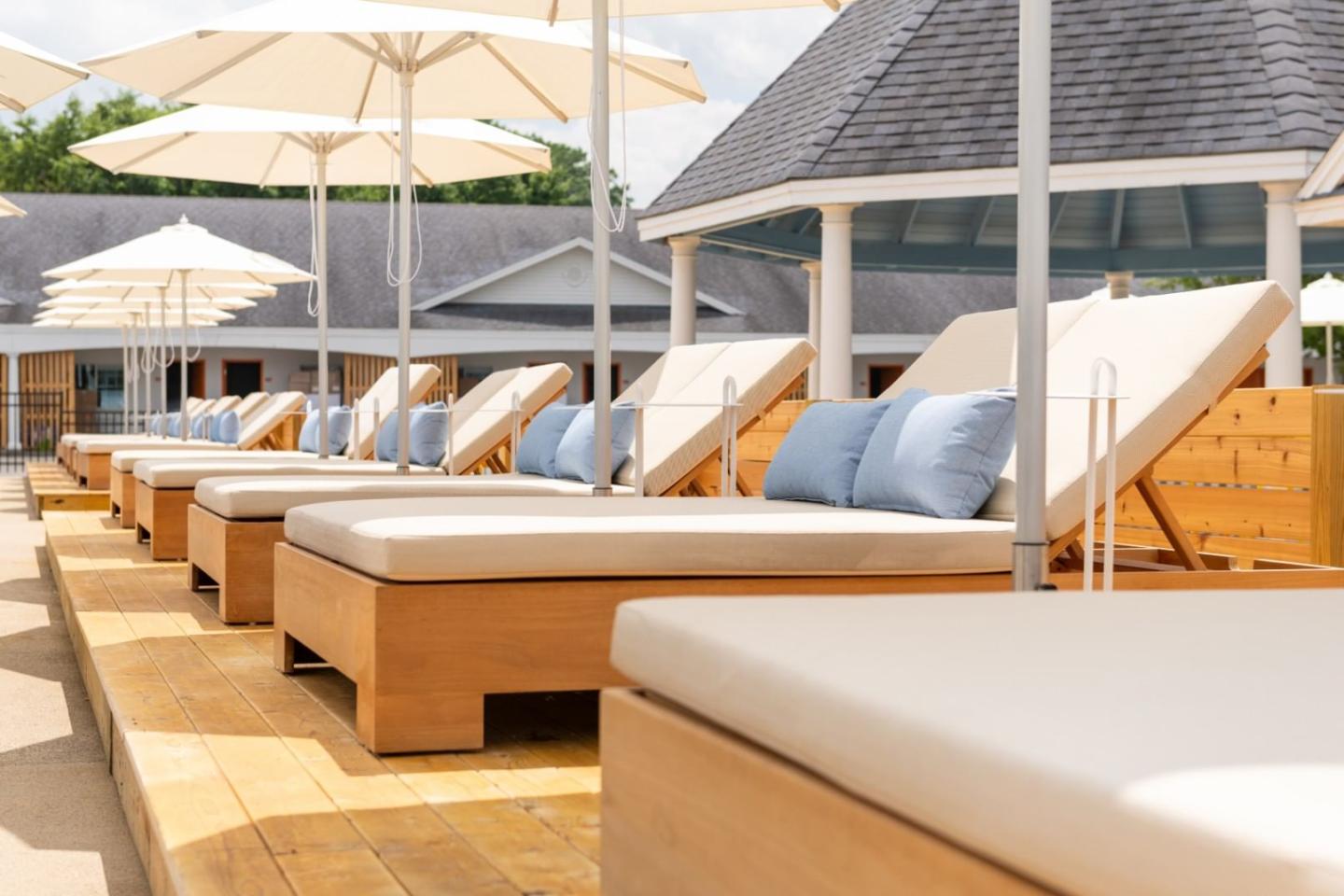 Sun loungers with white cushions under umbrellas on a wooden deck.