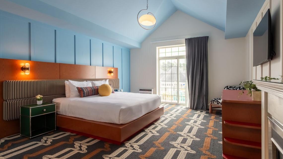 Hotel room with a modern design, blue walls, and patterned carpet. Large bed and window.