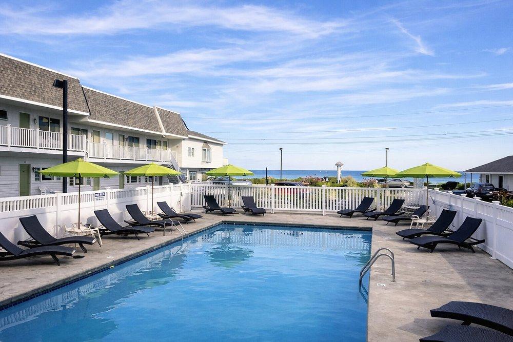 Hotel pool with green umbrellas, lounge chairs, and ocean view.