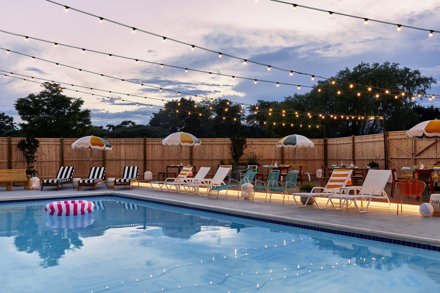 Poolside with loungers, umbrellas, and string lights at dusk.