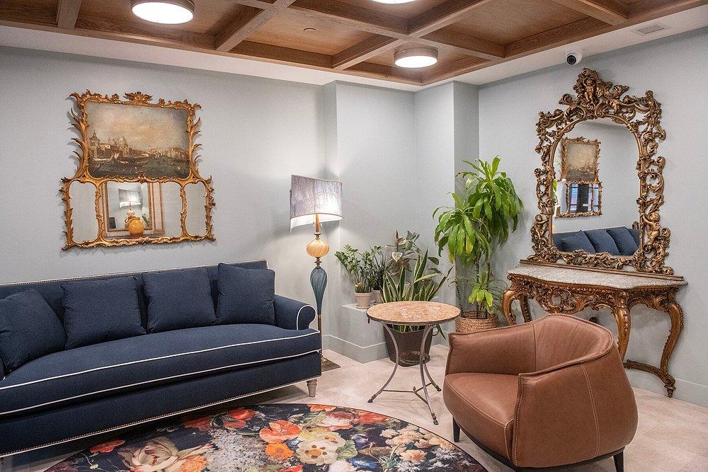 Elegant living room with blue sofa, ornate mirror, plants, and floral rug.