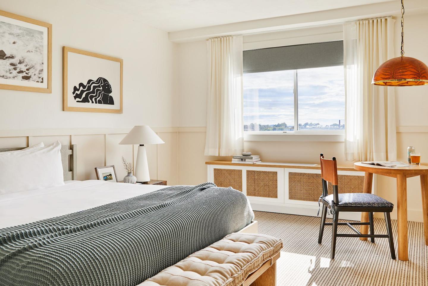 Bright bedroom with a large bed, window, desk, and artwork on walls.