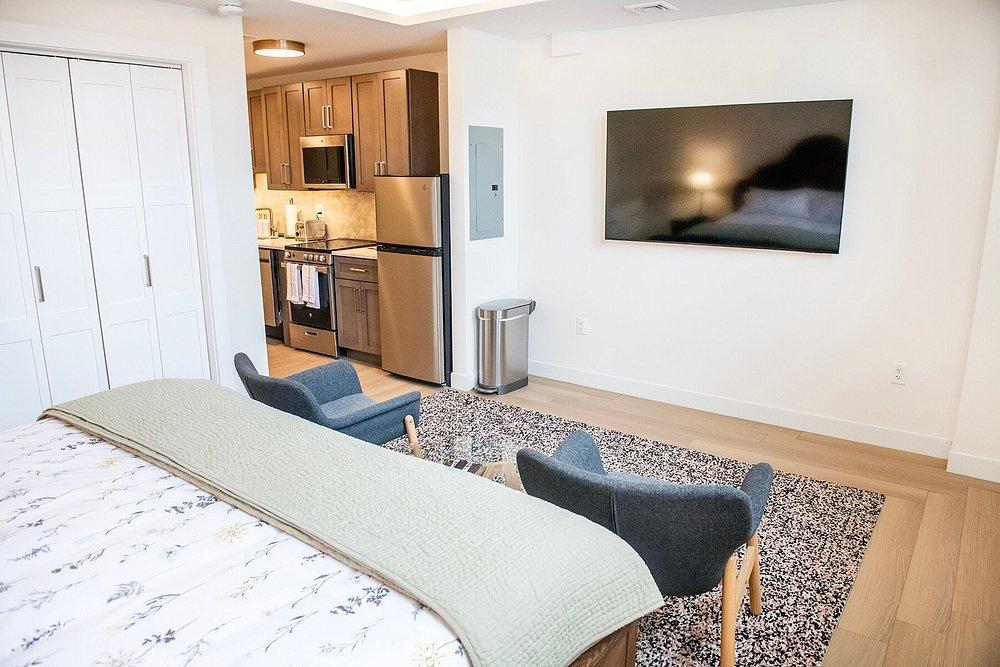 Hotel room with bed, TV, two chairs, and kitchenette.