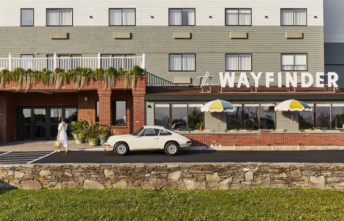 Hotel entrance with white car parked, woman walking on sidewalk.