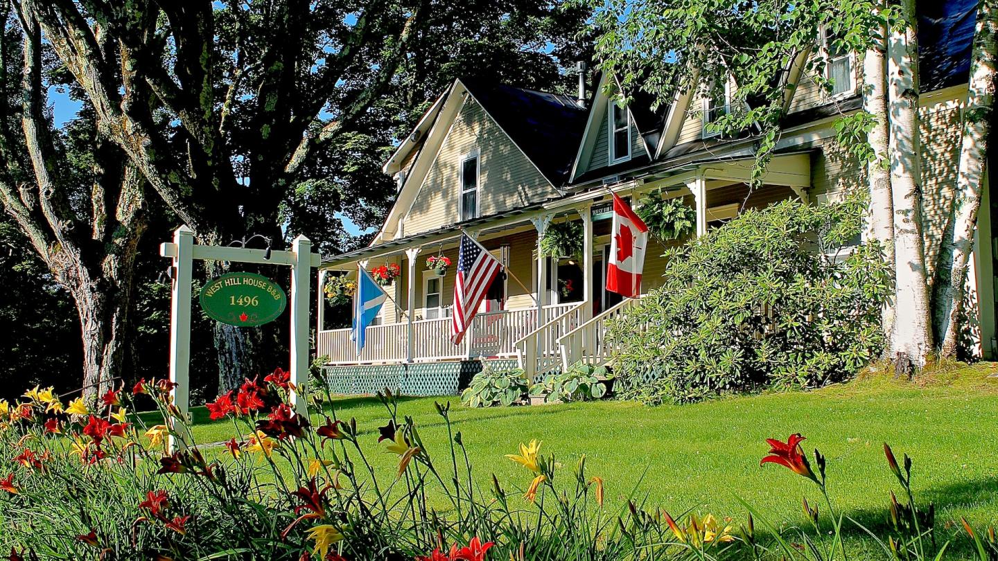 Charming house with flags and vibrant garden, surrounded by lush greenery.