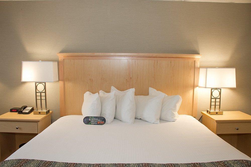 Bed with white pillows, remote on blanket, flanked by wooden nightstands and lamps.