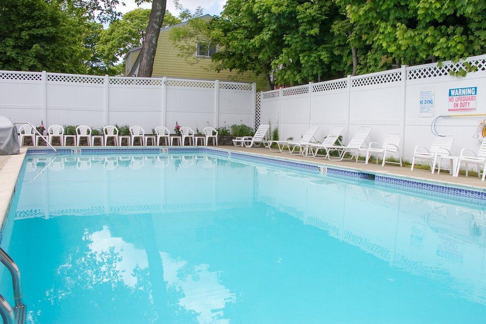 Outdoor swimming pool with white lounge chairs and trees nearby.