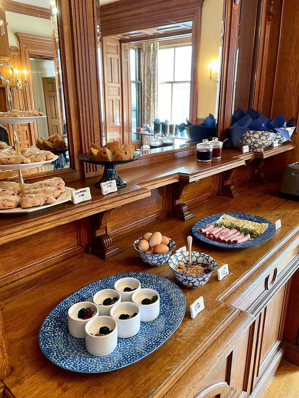 Breakfast buffet with pastries, eggs, yogurt cups, and cold cuts on a wooden counter.