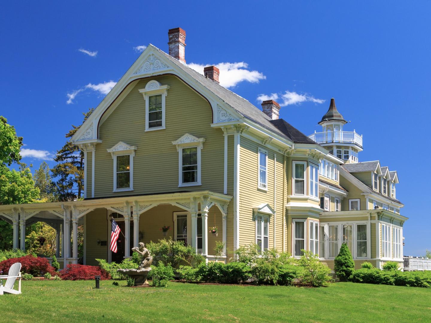 Victorian-style house with turret, lush garden, under clear blue sky.