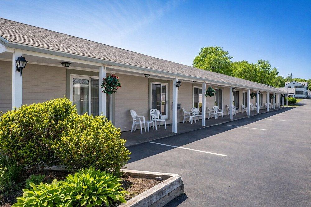 Single-story motel with white columns and chairs, surrounded by greenery.