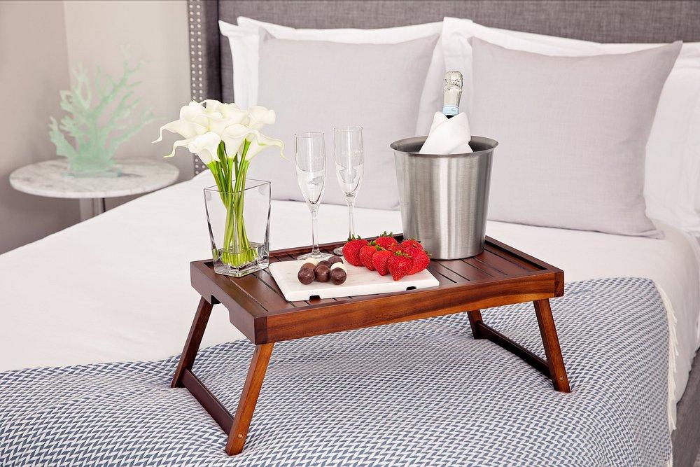Breakfast tray on bed with flowers, champagne, glasses, strawberries, and chocolates.