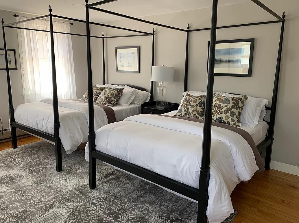 Two four-poster beds with white bedding in a bright room with framed art.