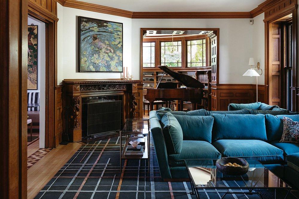 Luxurious living room with teal sofa, fireplace, and a grand piano in the background.
