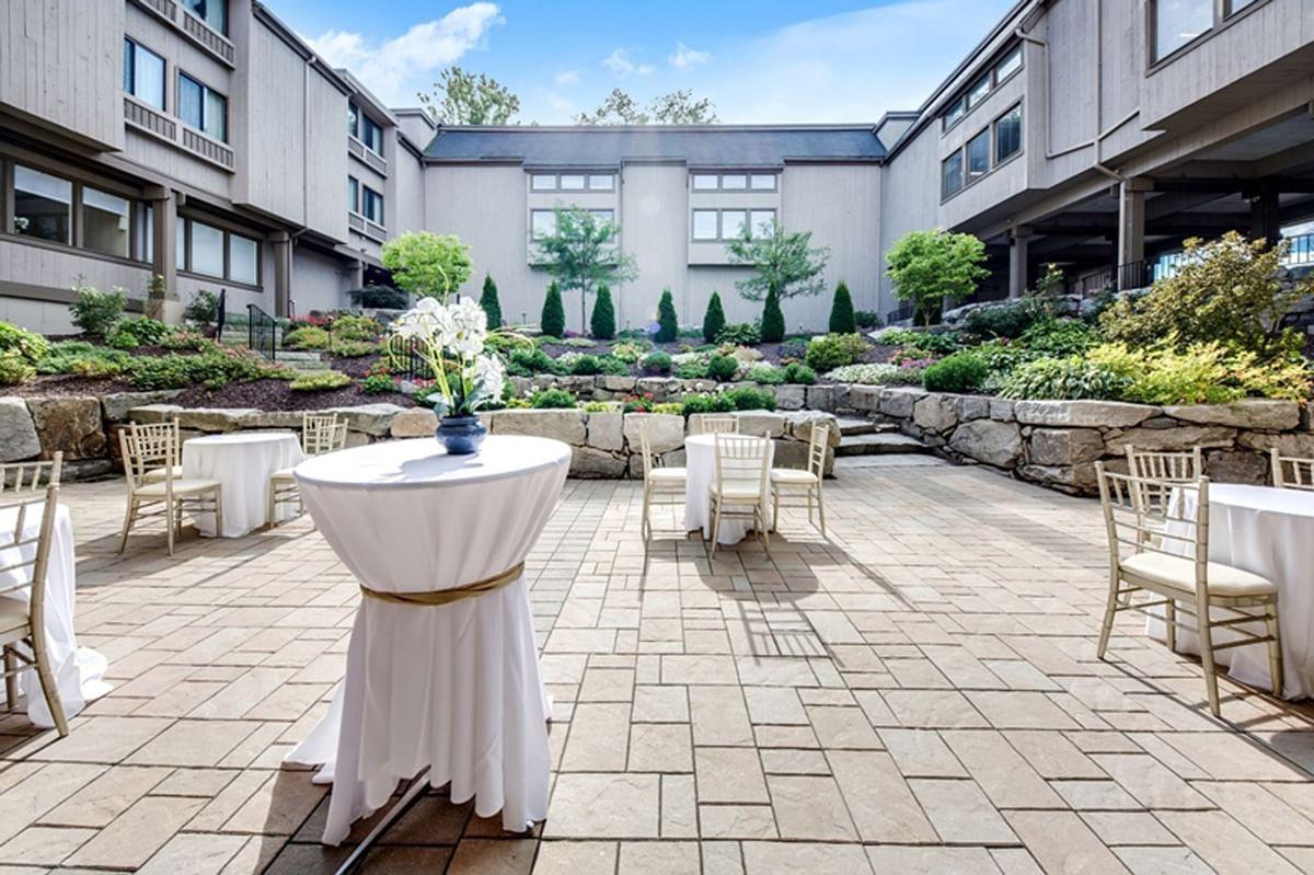 Courtyard with round tables, white cloths, and potted plants.