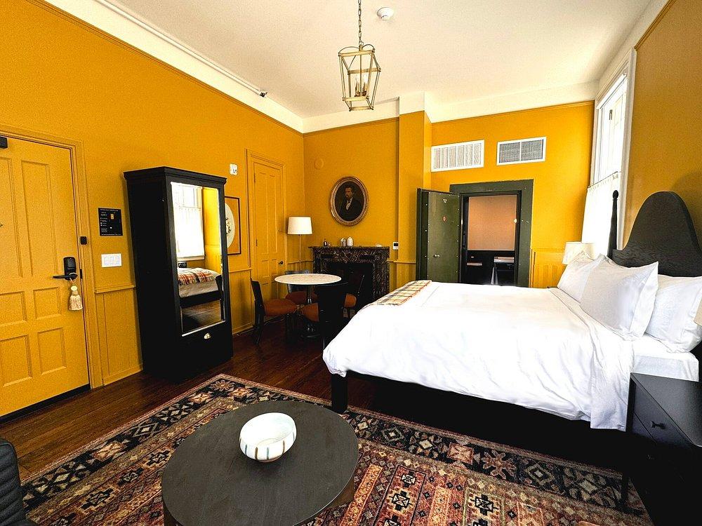 Cozy yellow hotel room with a bed, table, and mirror.
