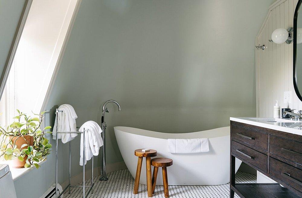 Attic bathroom with a modern bathtub, wooden stools, plants, and a vanity.