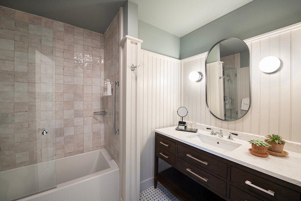 Bathroom with tub, oval mirror, and dual sinks on a dark wood vanity.