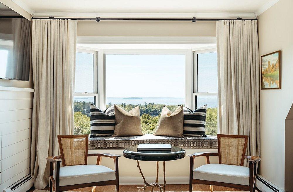Cozy sunlit room with chairs and a window seat overlooking a scenic view.