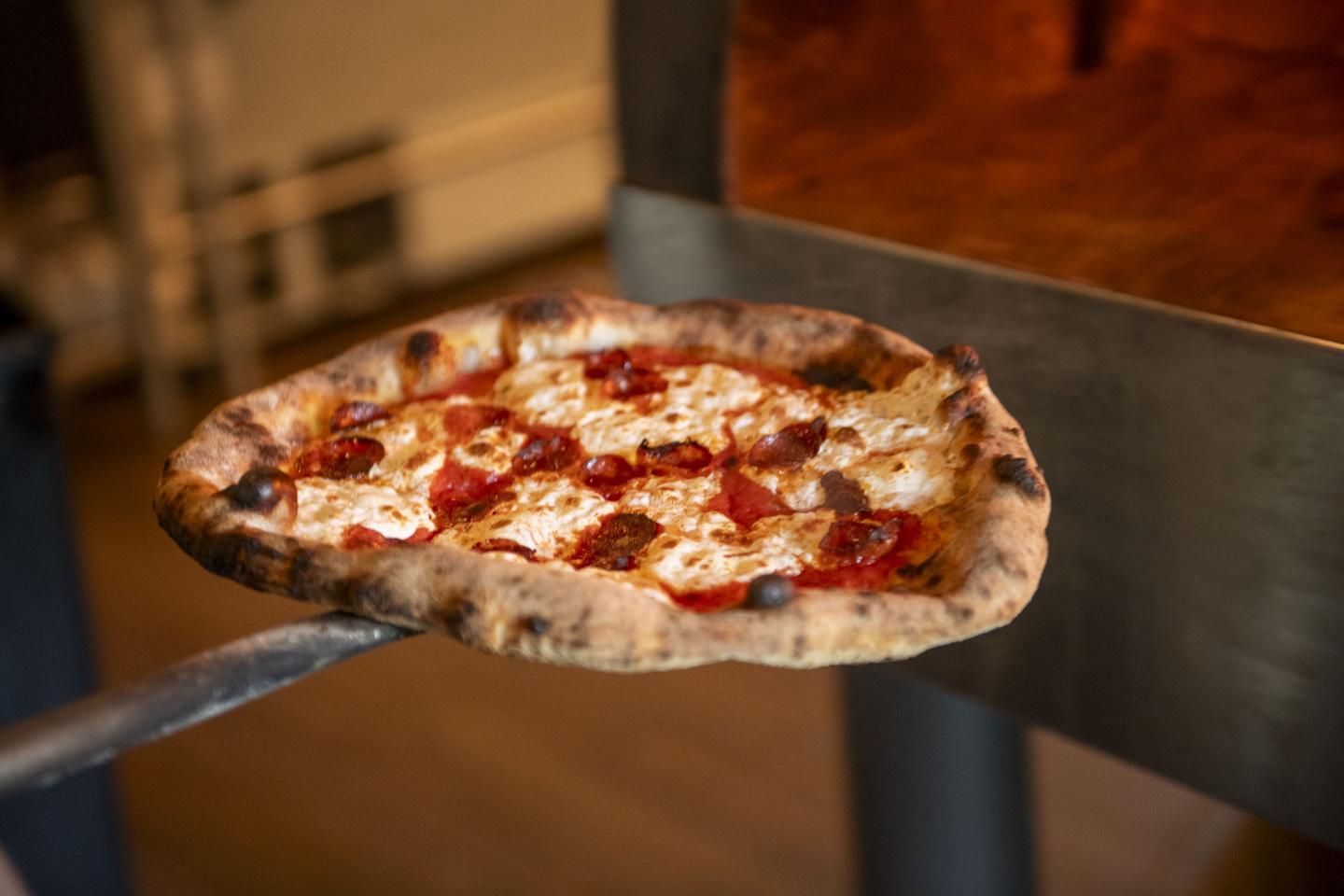 Wood-fired pizza with cheese and pepperoni on a metal paddle.