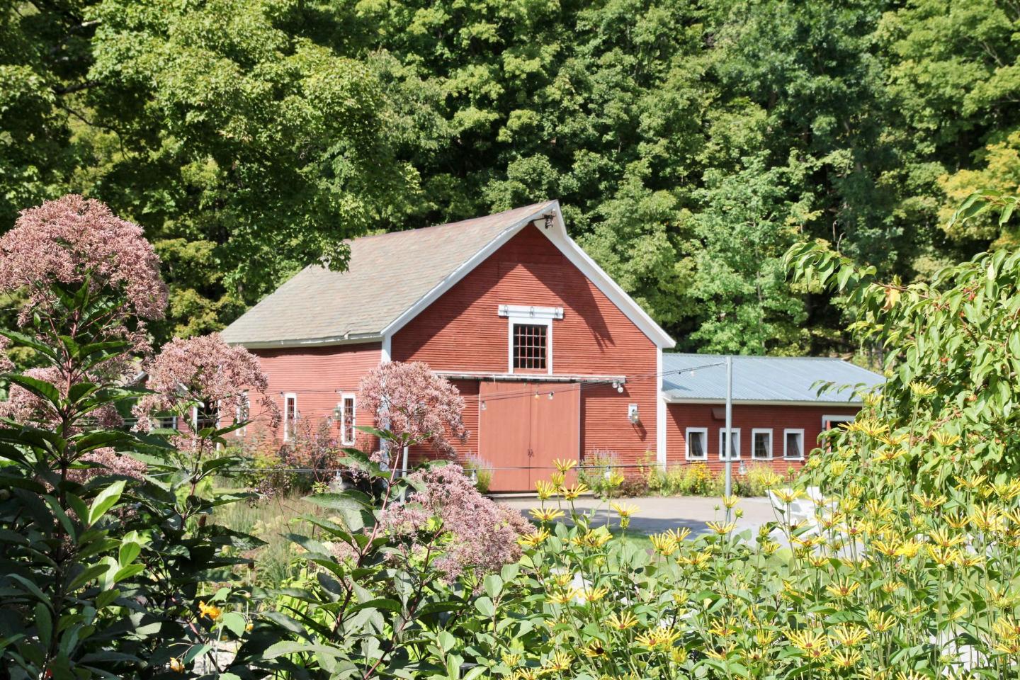 Red barn surrounded by lush greenery and flowering plants.